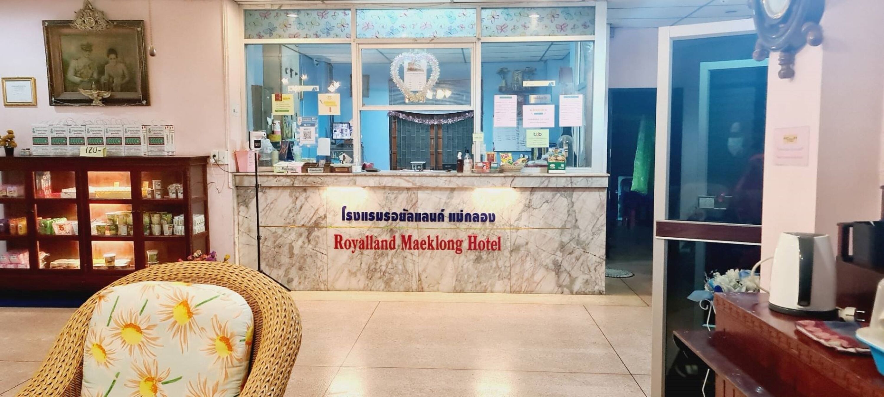 A reception desk with a sign reading "Royalland Maeklong Hotel" and a display of various items.