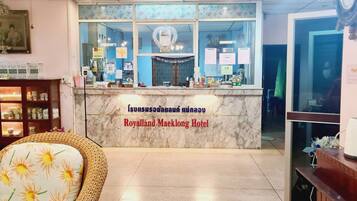 A reception desk with a sign reading "Royalland Maeklong Hotel" and a display of various items.