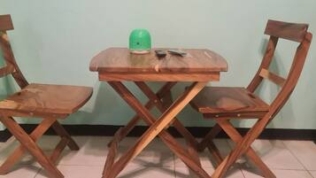 Una pequeña mesa de madera con dos sillas, una tetera verde y un control remoto encima.