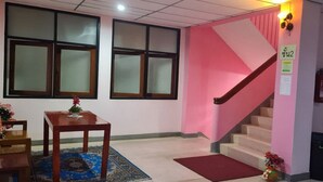 A staircase with a pink wall, a wooden table with a vase, and a rug. - Royal Land Mae Klong Hotel (Samut Songkhram)
