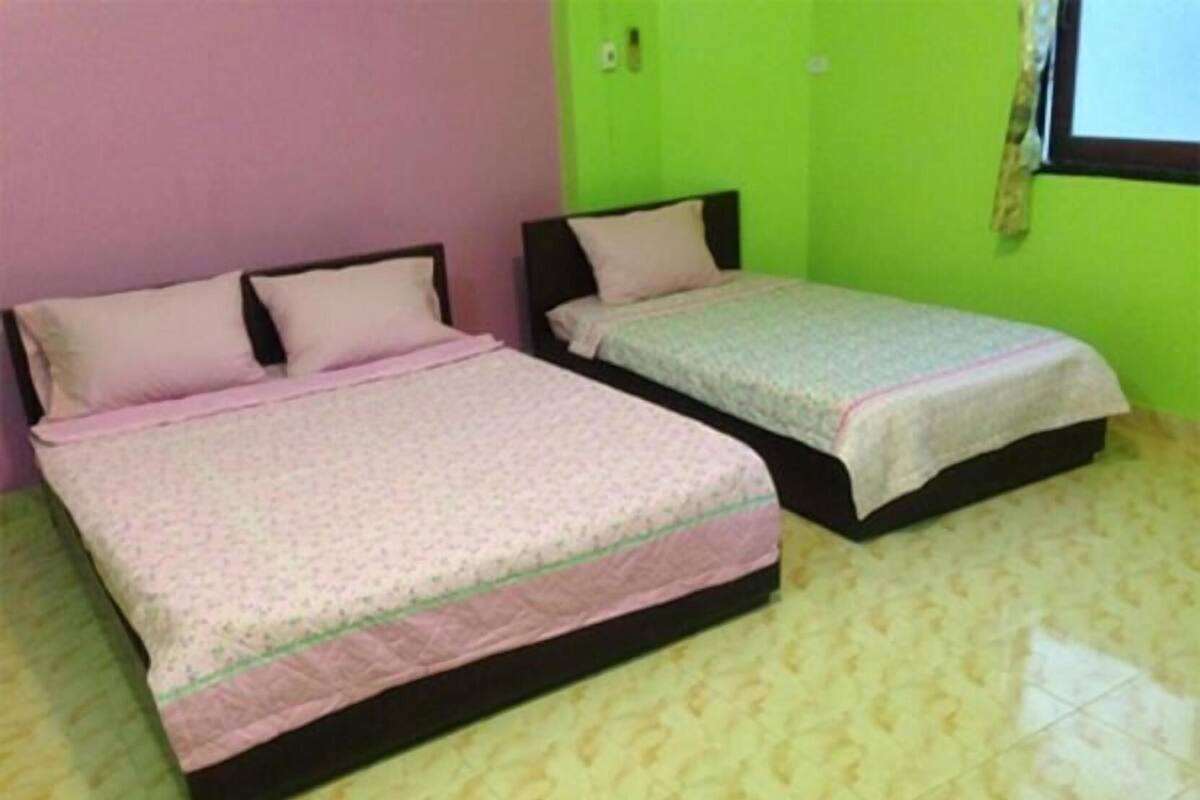 Two single beds with black frames and pink bedding, a green wall, and a tiled floor.