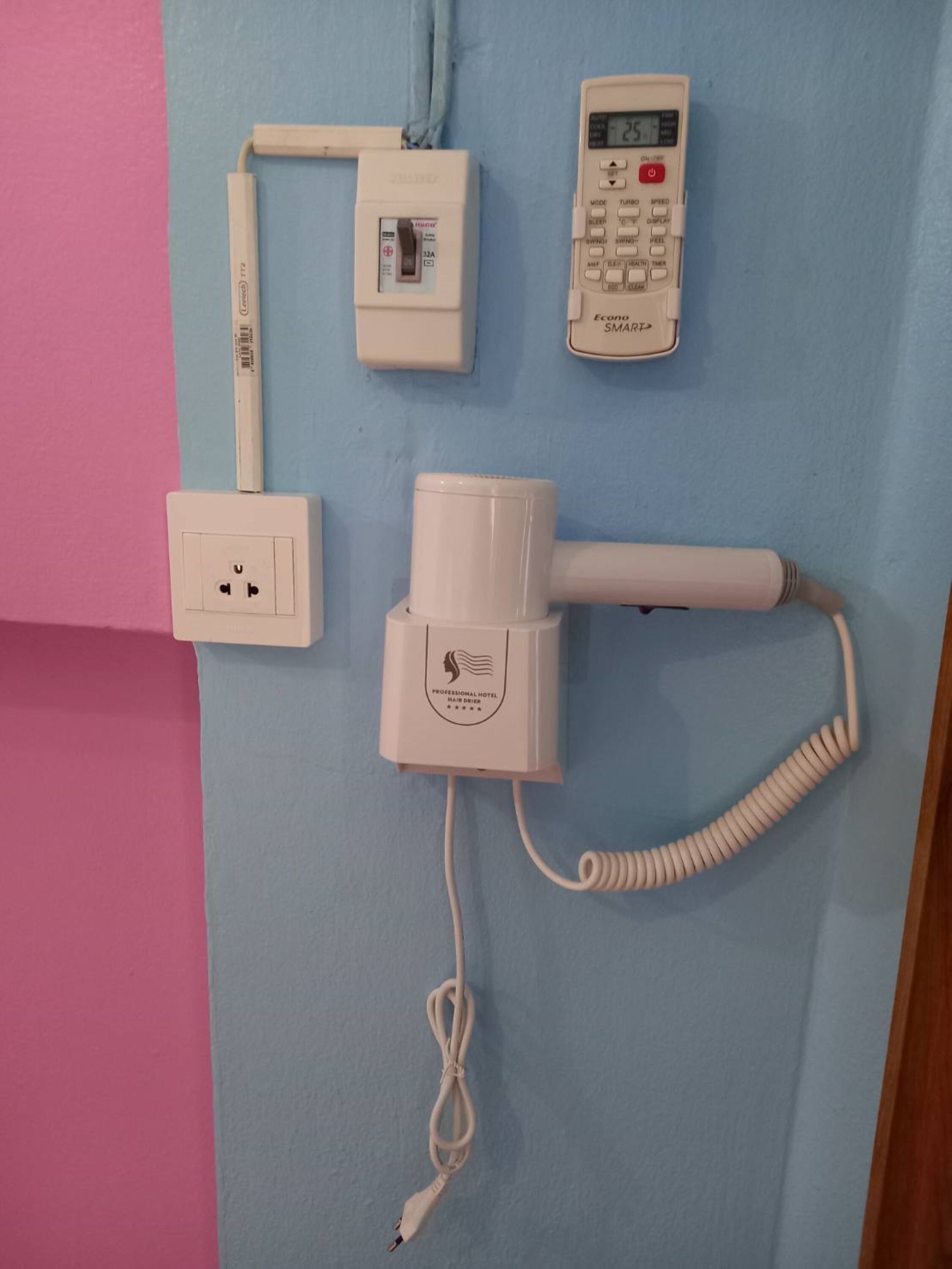 Ein Fön, eine Steckdose, ein Telefon und ein Schalter an einer blauen Wand.
