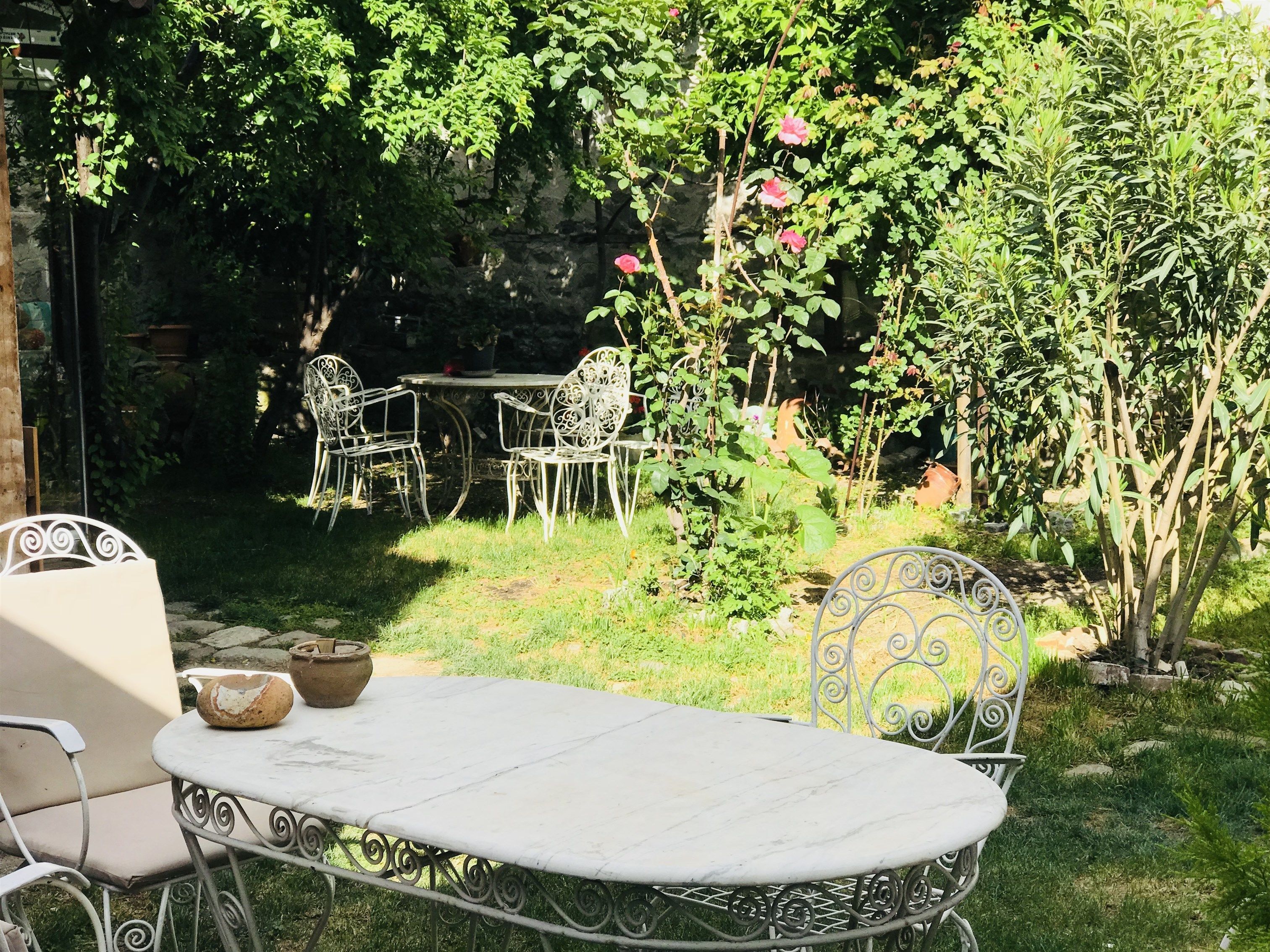 Eine Terrasse im Freien mit Tisch und Stühlen, umgeben von üppigem Grün und blühenden Pflanzen.