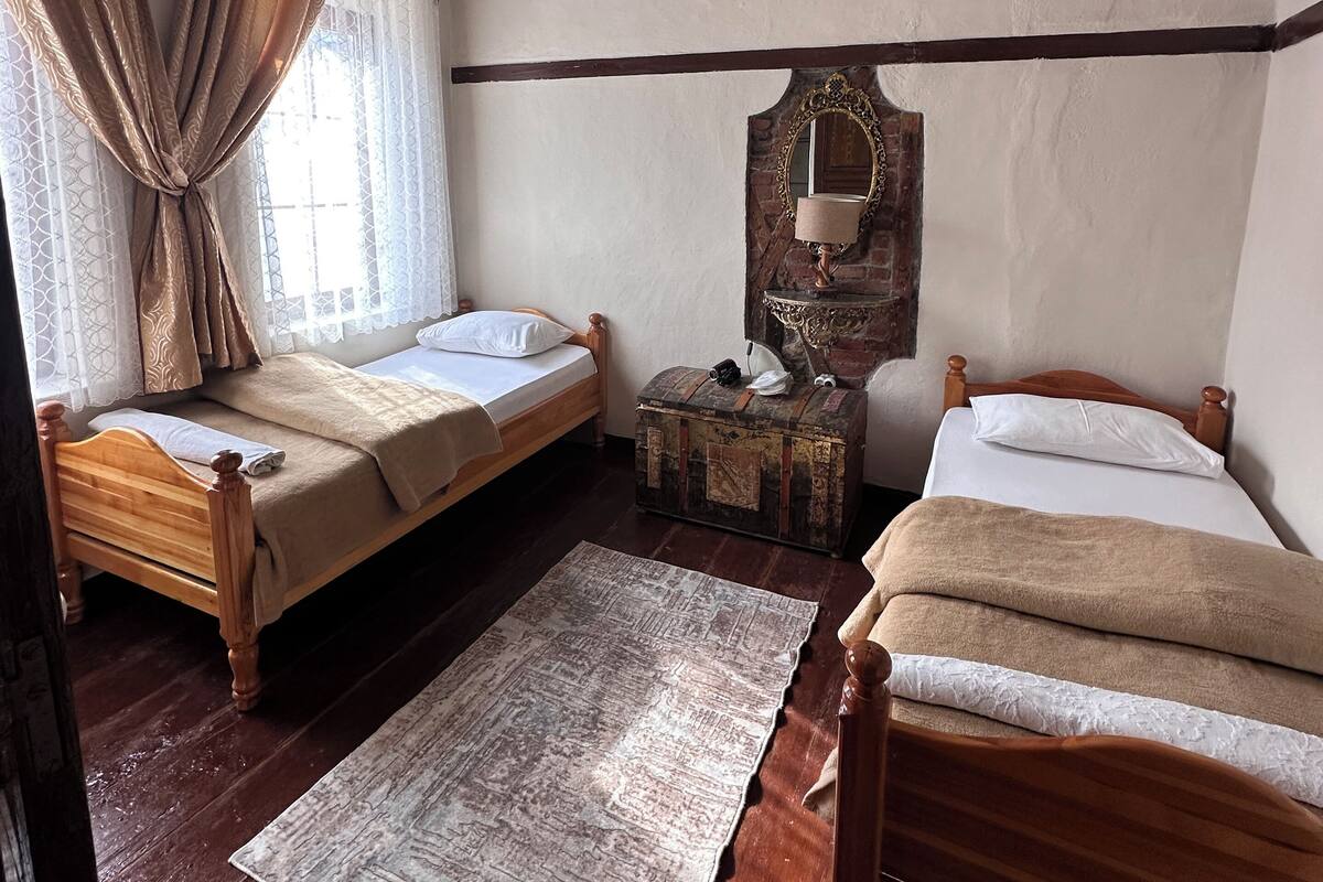 Ein Zimmer mit zwei hölzernen Betten, einer Truhe, einem Spiegel und einem Deckenventilator.