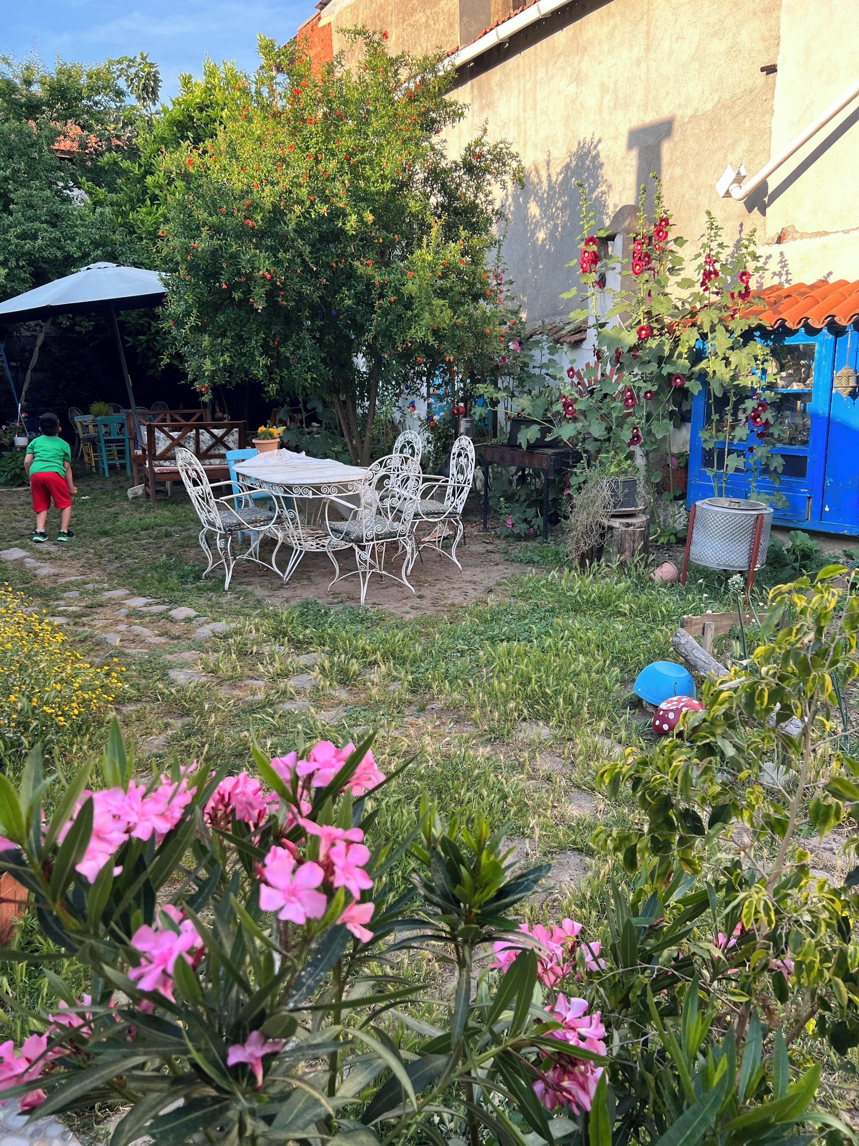 An outdoor seating area with a metal table and chairs, surrounded by greenery and flowers.