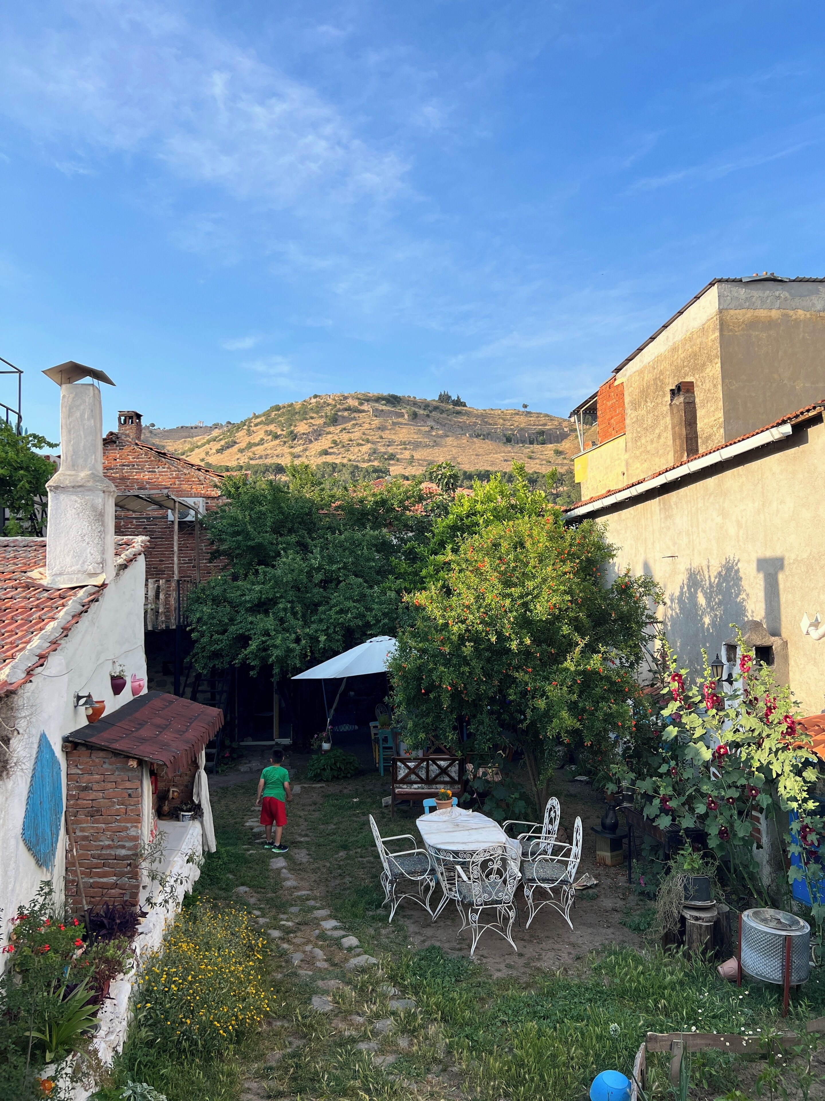 A courtyard with a table and chairs, surrounded by greenery and a view of hills.