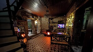 A dimly lit room with a patterned floor, stone walls, a wooden ceiling, a television, and a fireplace. - Pergamon Pension (Bergama)