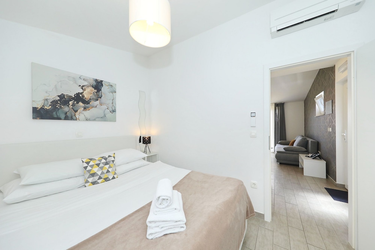 A hotel room with a bed, a bedside lamp, a painting, and an air conditioning unit.