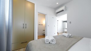 Une chambre d’hôtel équipée d’un lit, d’une armoire, d’un appareil de climatisation et d’une salle de bain visible à travers une porte ouverte.
