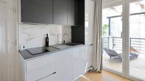 Une cuisine moderne avec un pare-feu en marbre, un plan de travail noir et une porte-fenêtre coulissante donnant sur un balcon aménagé avec des sièges d’extérieur.