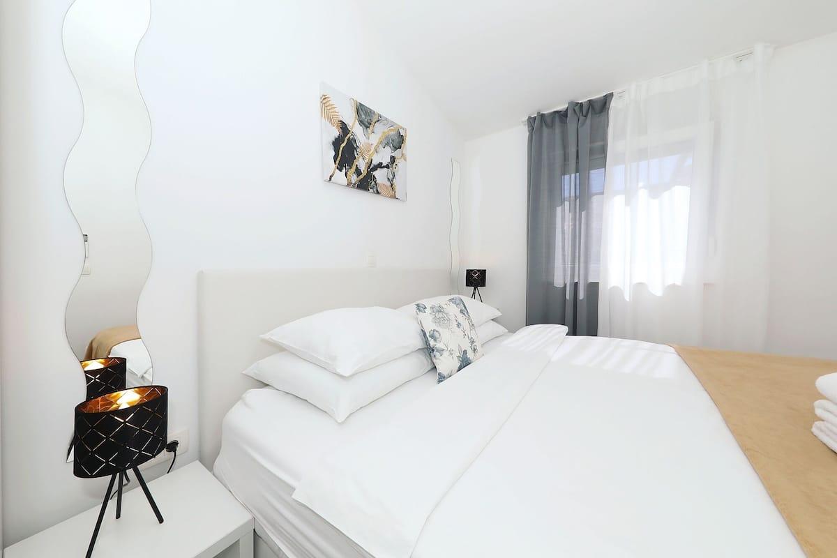 A modern bedroom with a bed, a nightstand, a lamp, a wall-mounted artwork, and a window with curtains.