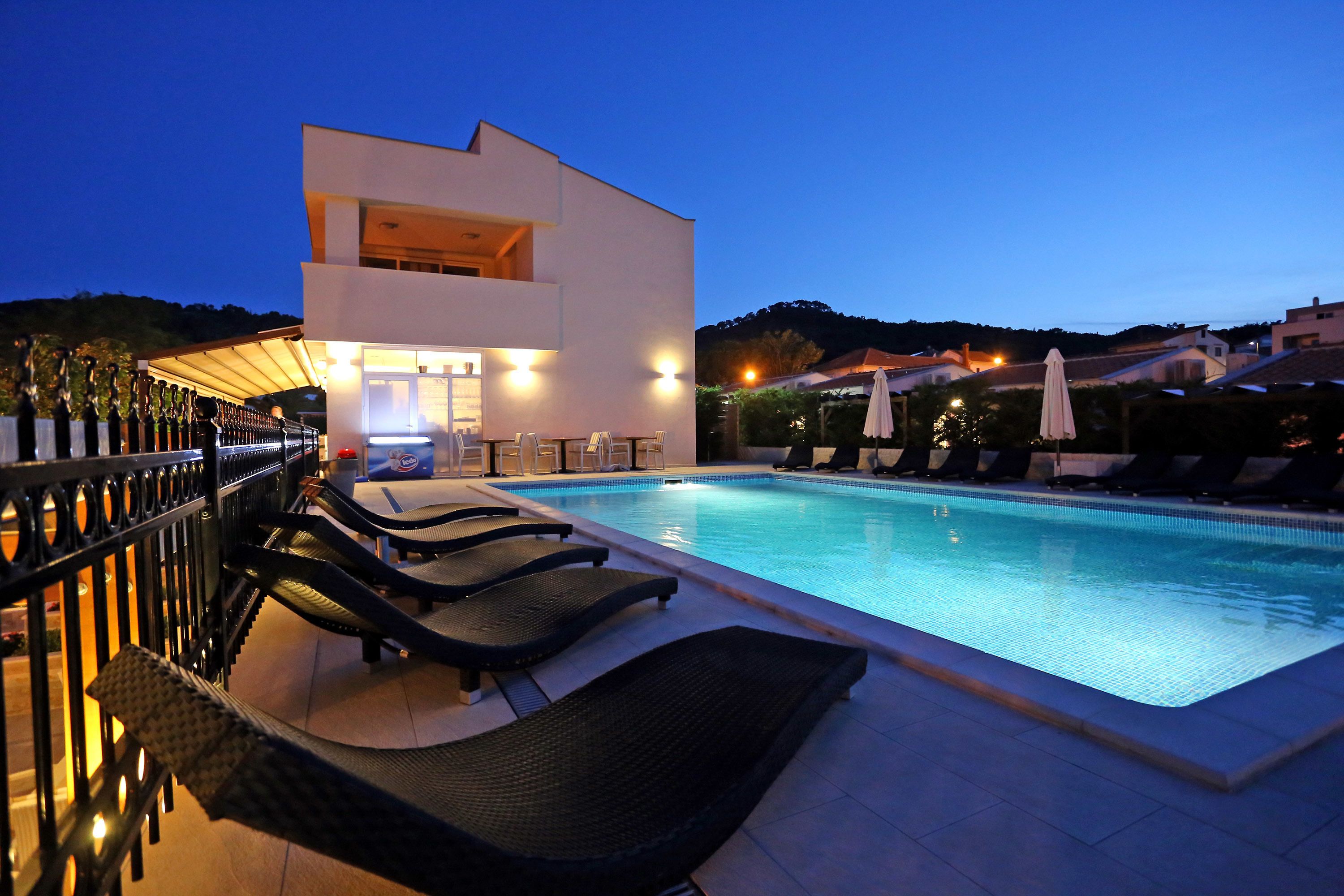 A modern pool area with lounge chairs, a pool, and a building with outdoor lighting.