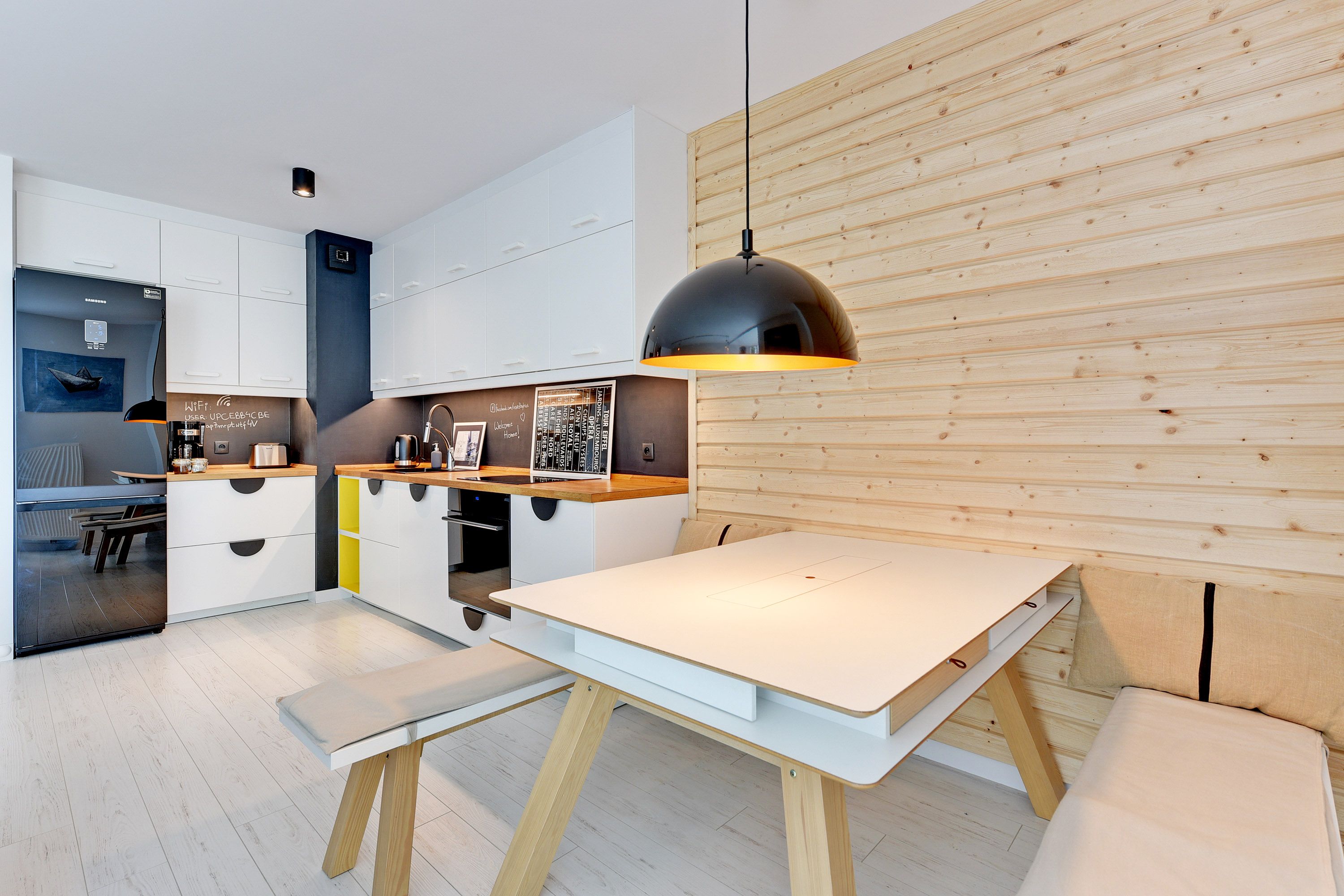 A modern kitchen with white cabinets, a wooden wall, and a pendant light above a white table.