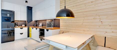 Cocina moderna con armarios blancos, pared de madera y una lámpara colgante sobre una mesa blanca.
