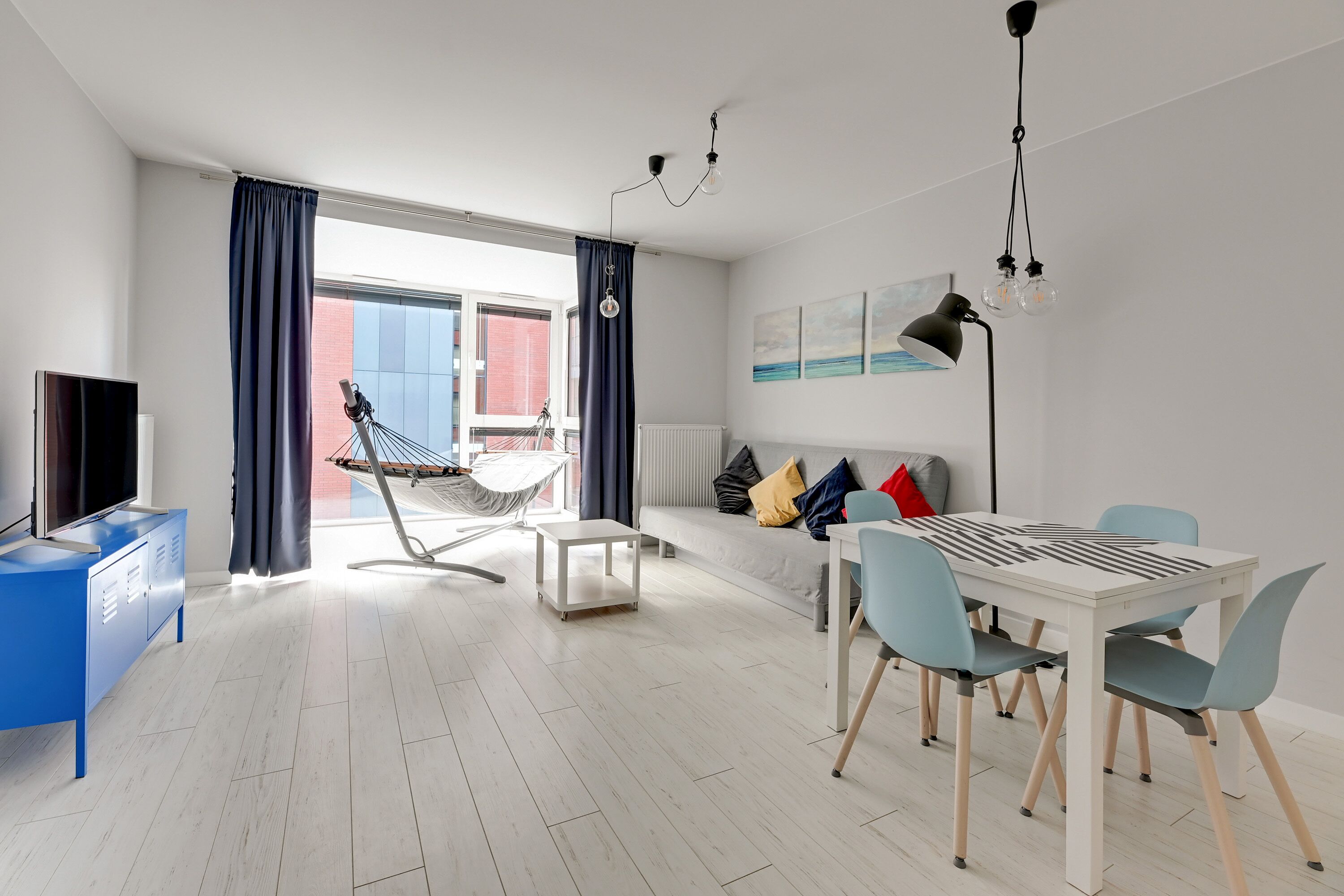 A modern living room with a dining table, chairs, a sofa, a TV, and a hammock.