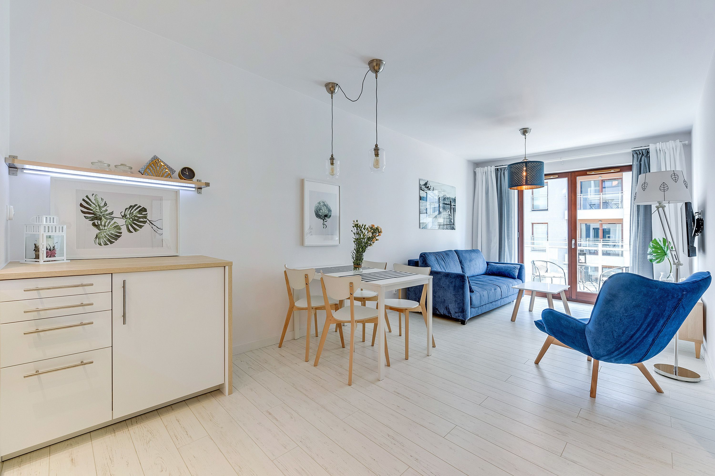A modern living room with a dining area, a blue sofa, and a blue chair.