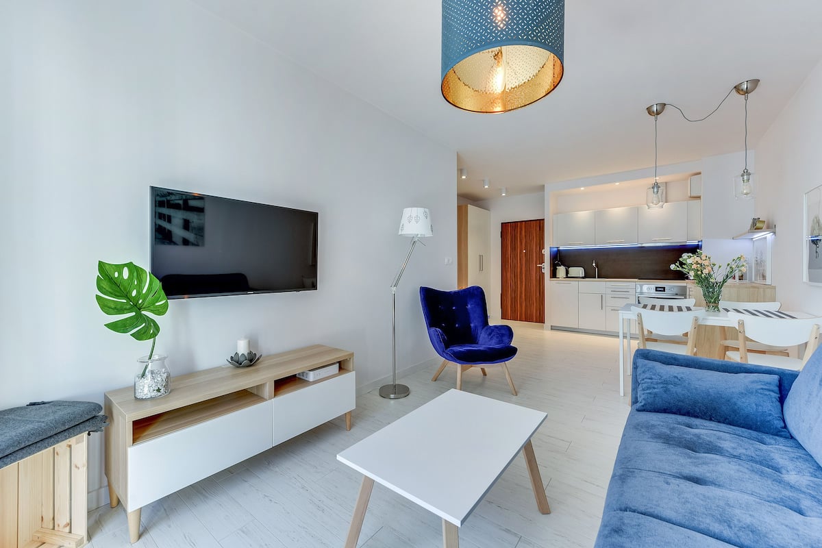 Een moderne woonkamer met een flatscreen televisie, een blauwe bank, een witte salontafel en een blauwe fauteuil.