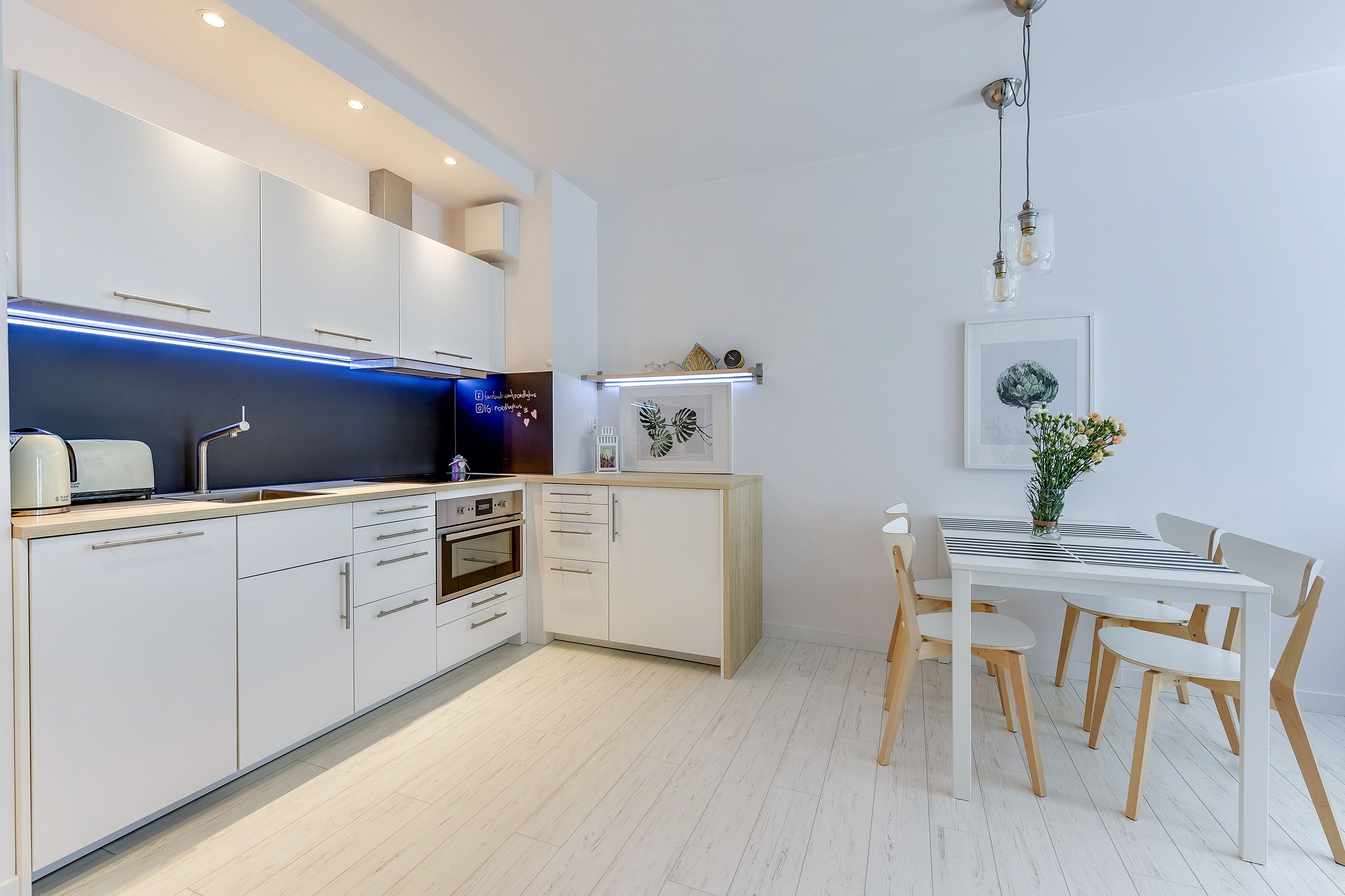A modern kitchen with white cabinetry, a built-in oven, and a dining area with a white table and chairs.