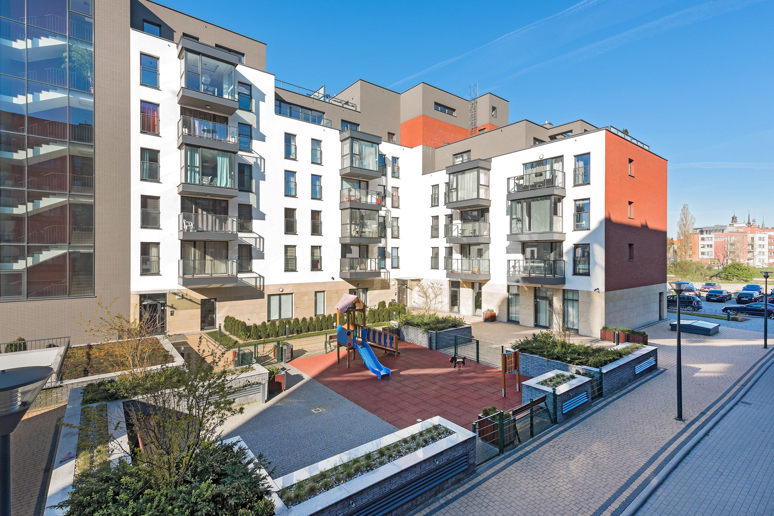 A modern apartment building with multiple balconies, a playground, and a parking area.