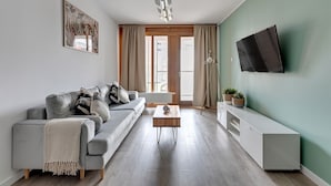 A modern living room with a grey sofa, a coffee table, and a TV mounted on the wall. - NORDBYHUS Apartamenty Chmielna Park (Gdansk)