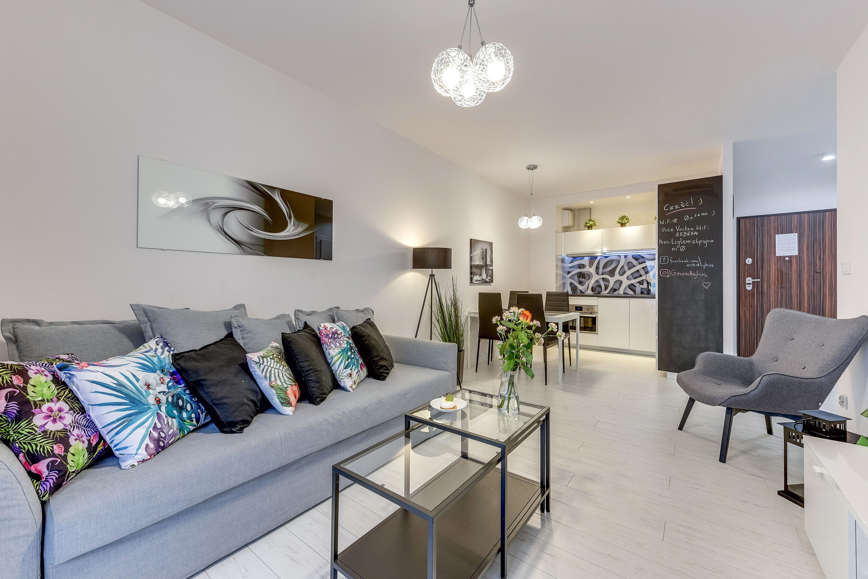 Un salon moderne avec un canapé gris, des coussins colorés, une table basse en verre et un fauteuil gris.