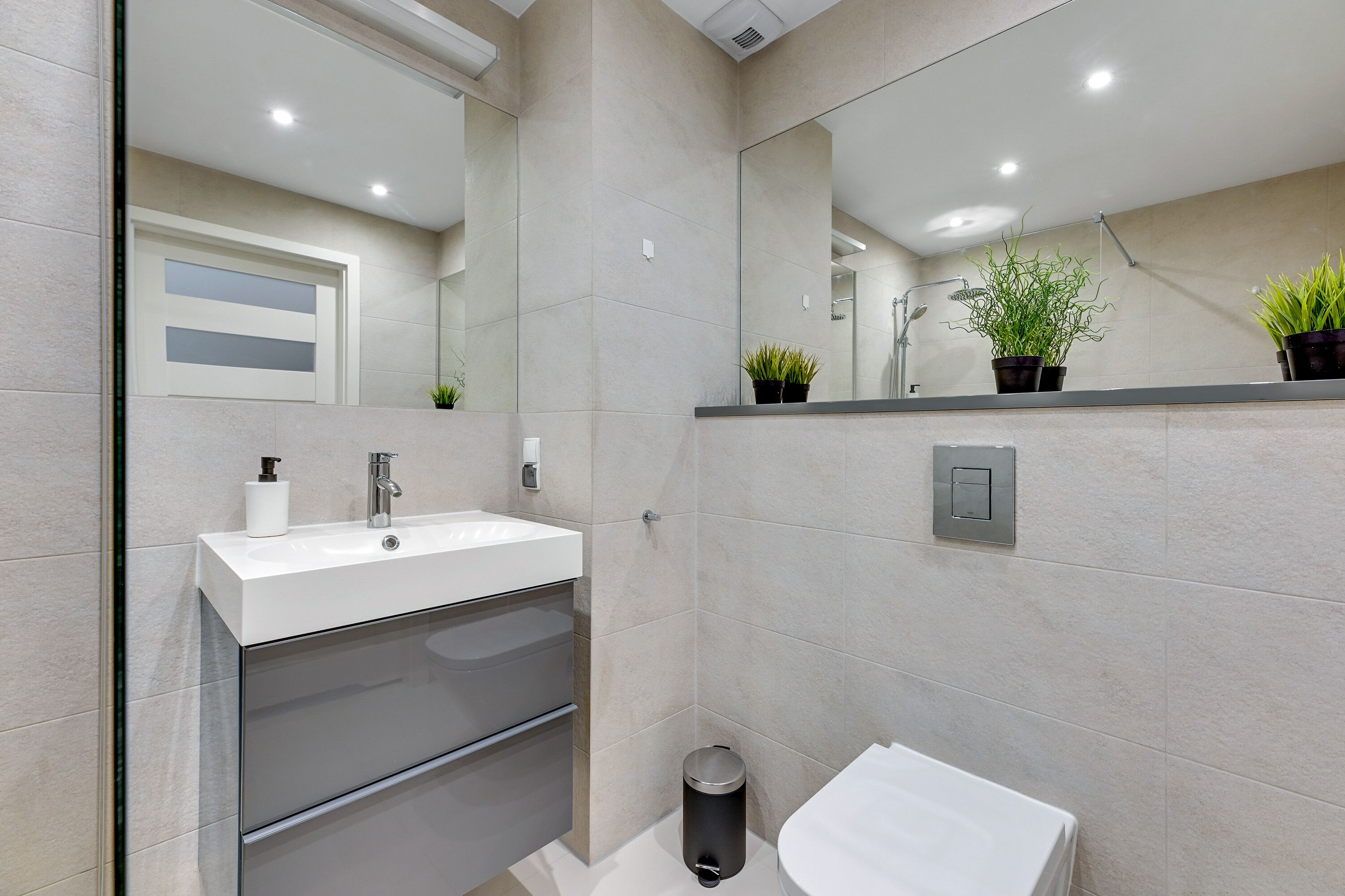 Un baño moderno con un lavabo blanco, espejo y un pequeño cubo de basura.