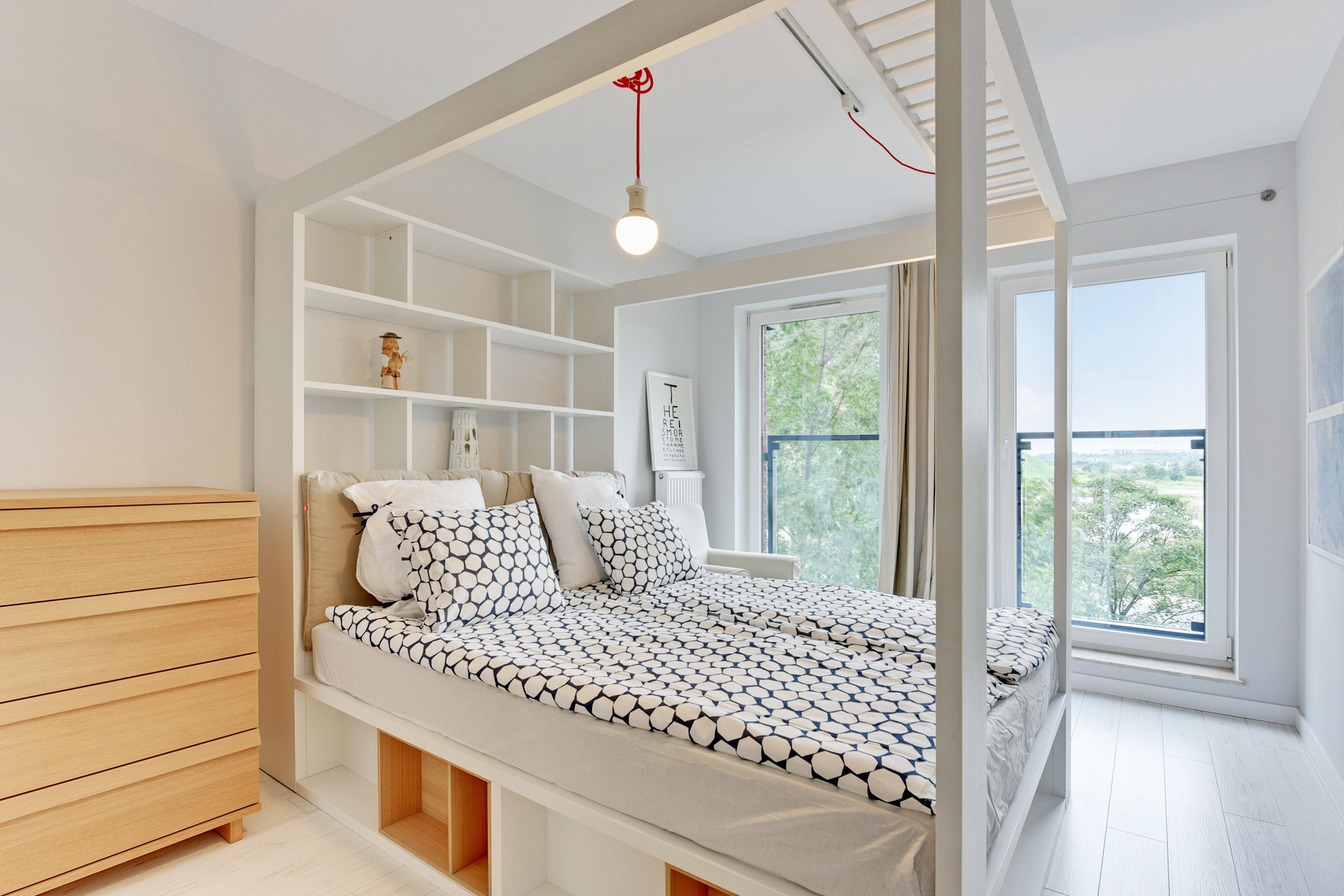 A modern bedroom with a built-in bed, white shelving, a window with a view, and a hanging light fixture.