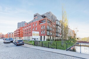Un edificio moderno con un cartel que indica que es un hotel. Hay coches aparcados delante, una zona pavimentada y un río al fondo.