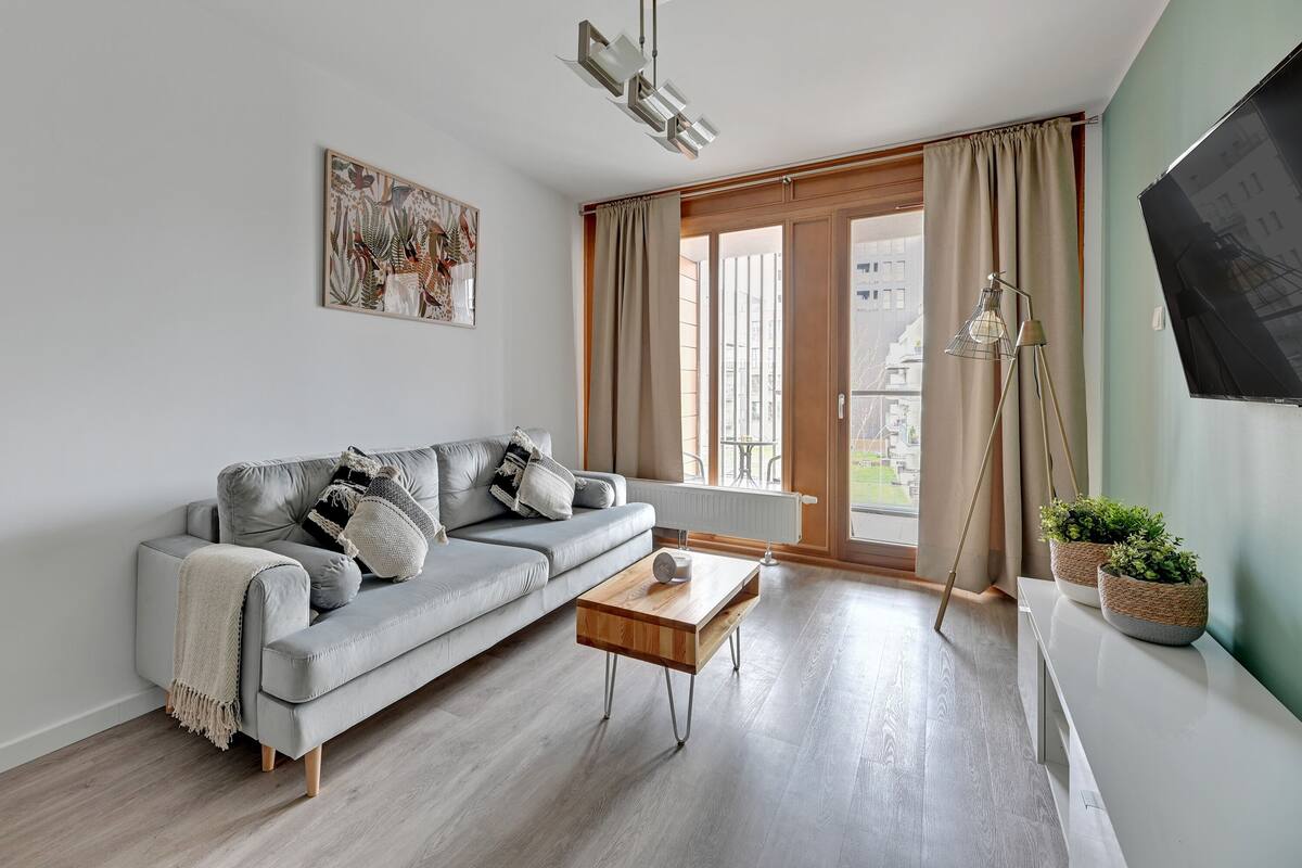 Een moderne woonkamer met een grijze bank, een houten salontafel en een vloerlamp.