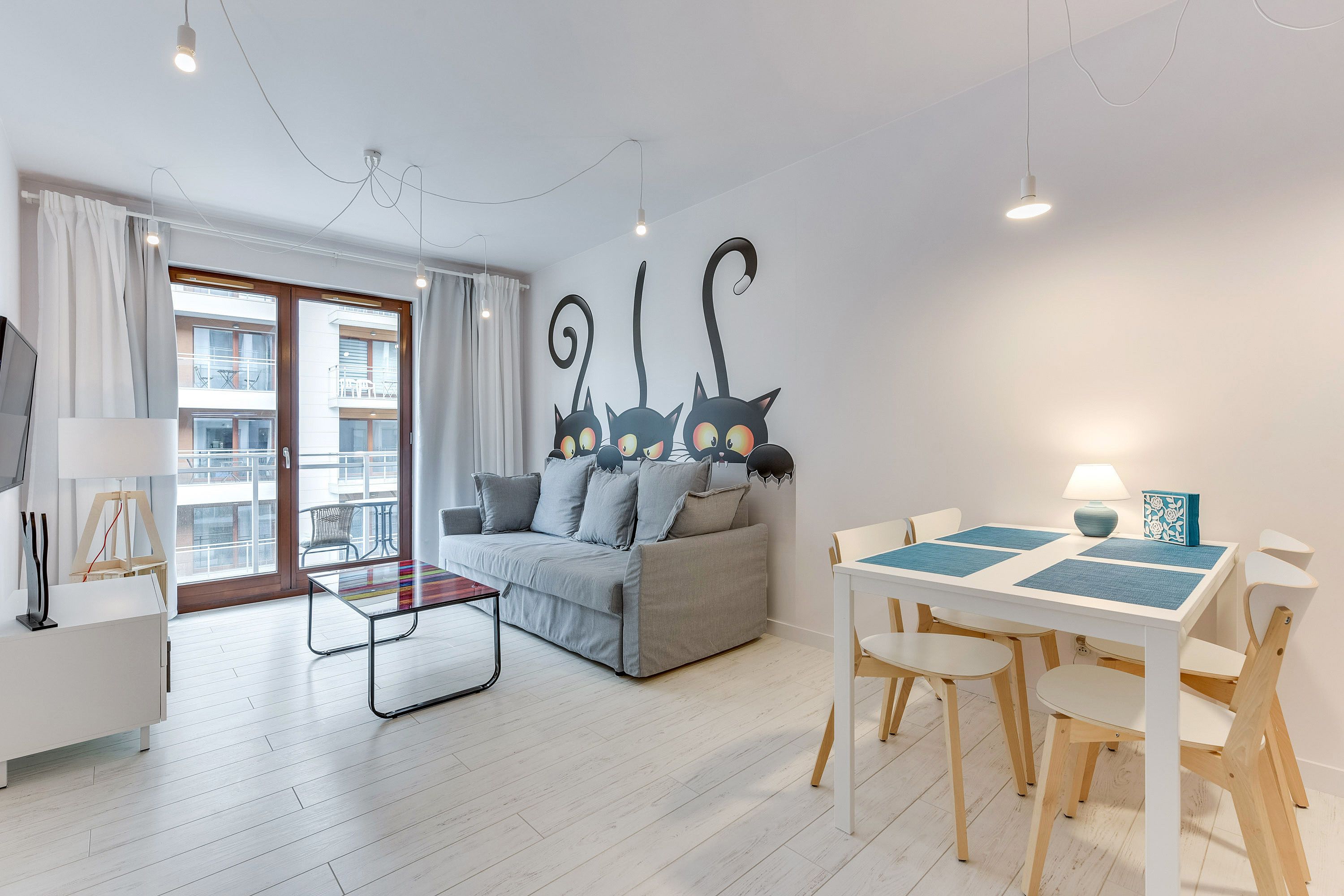 A modern living room with a grey sofa, a glass coffee table, and a dining area with a white table and wooden chairs.