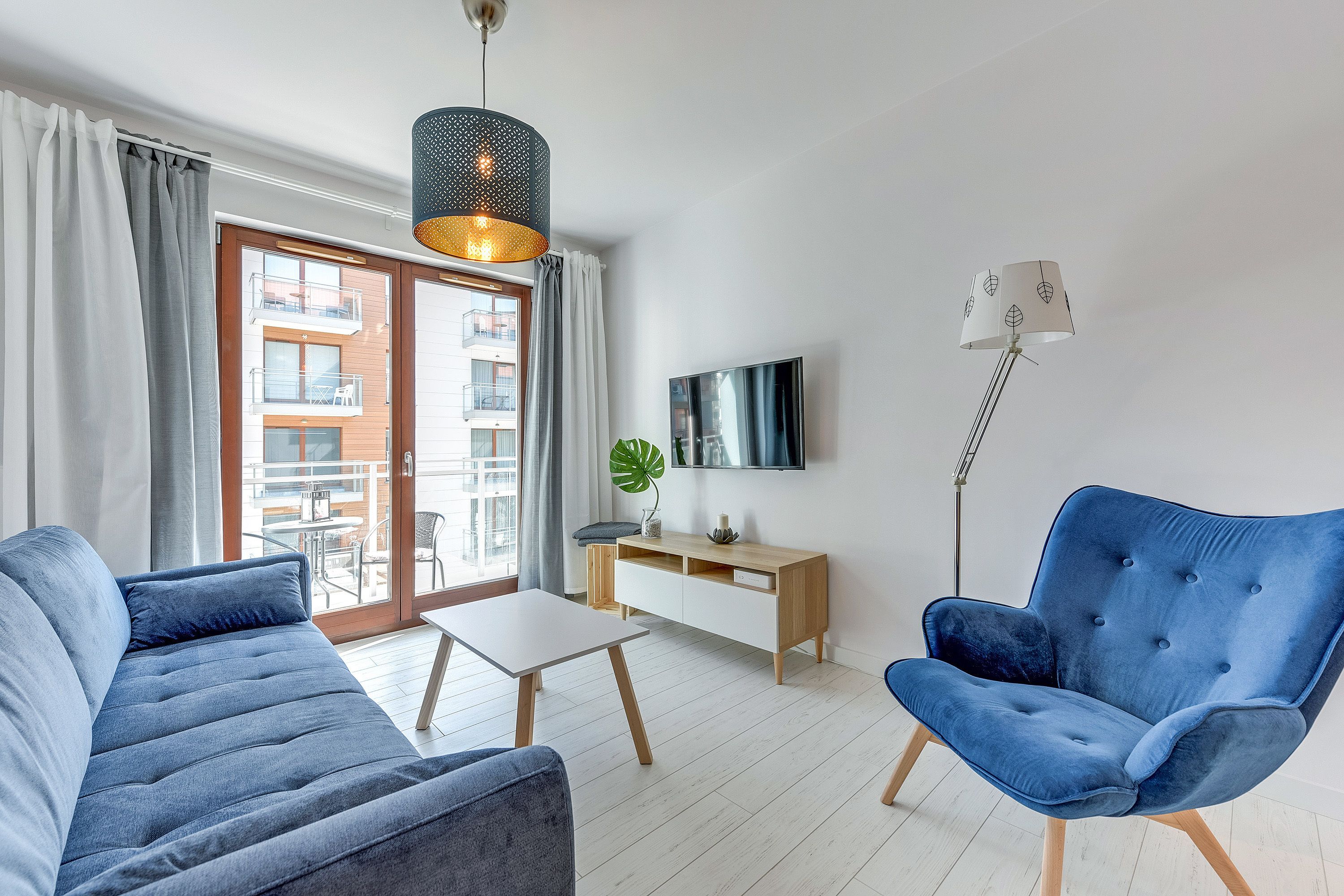 A modern living room with a sofa, a blue armchair, a small table, a TV, and a desk.