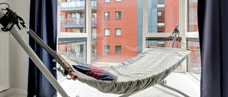 A balcony with a hammock and a view of a red brick building.