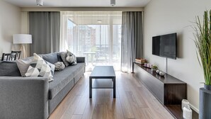 A modern living room with a grey sofa, a black coffee table, and a TV on the wall. - NORDBYHUS Apartamenty Chmielna Park (Gdansk)
