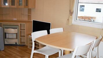 Een compacte keuken met houten kastjes, een eettafel met witte stoelen en een raam met uitzicht op een gebouw.