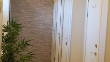 A narrow hallway with a bamboo plant on the left, a brick wall, and white doors on the right.
