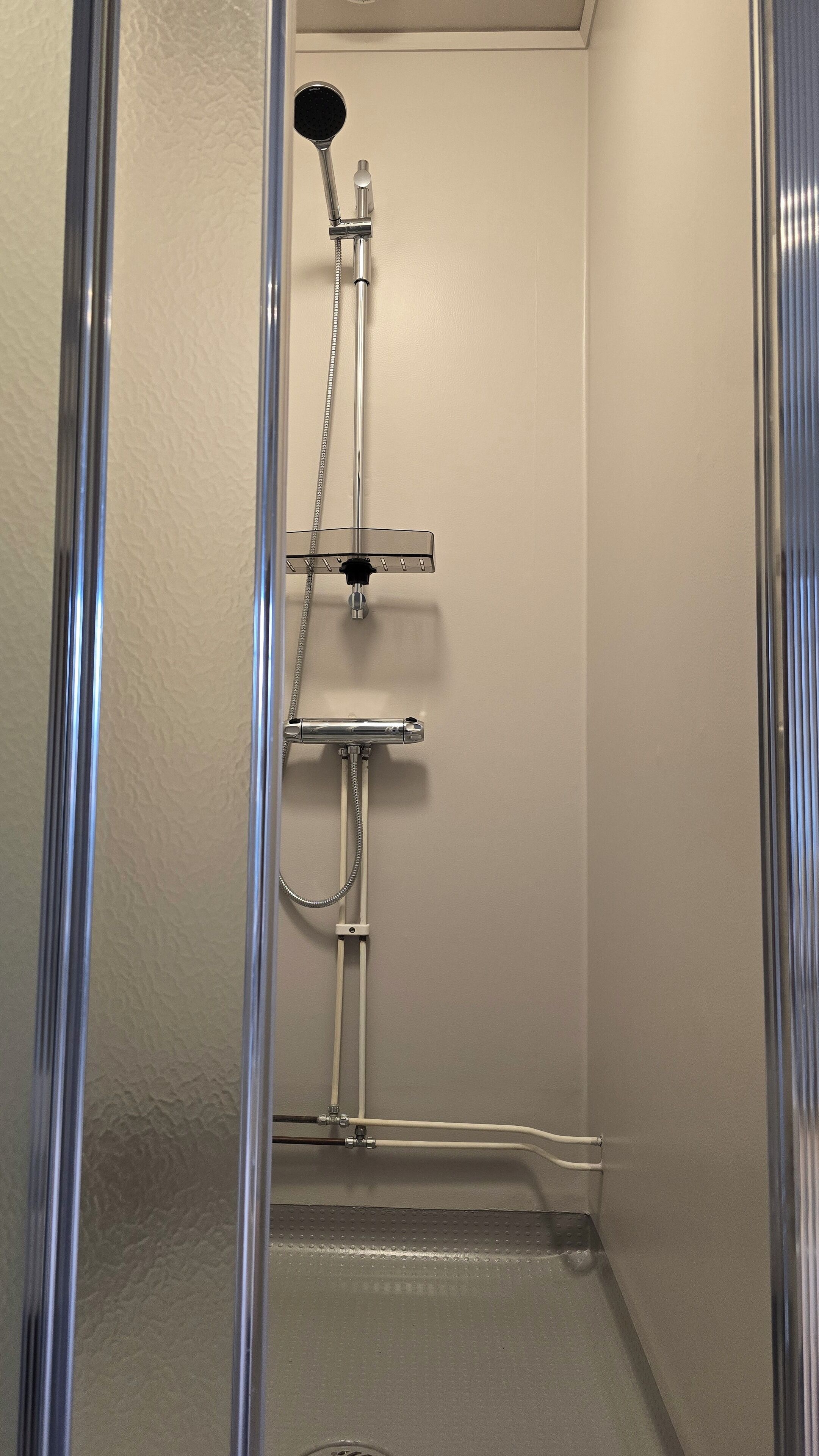En dusch med ett duschhuvud som kan hållas i handen, en väggmonterad kontrollpanel och ett avlopp.