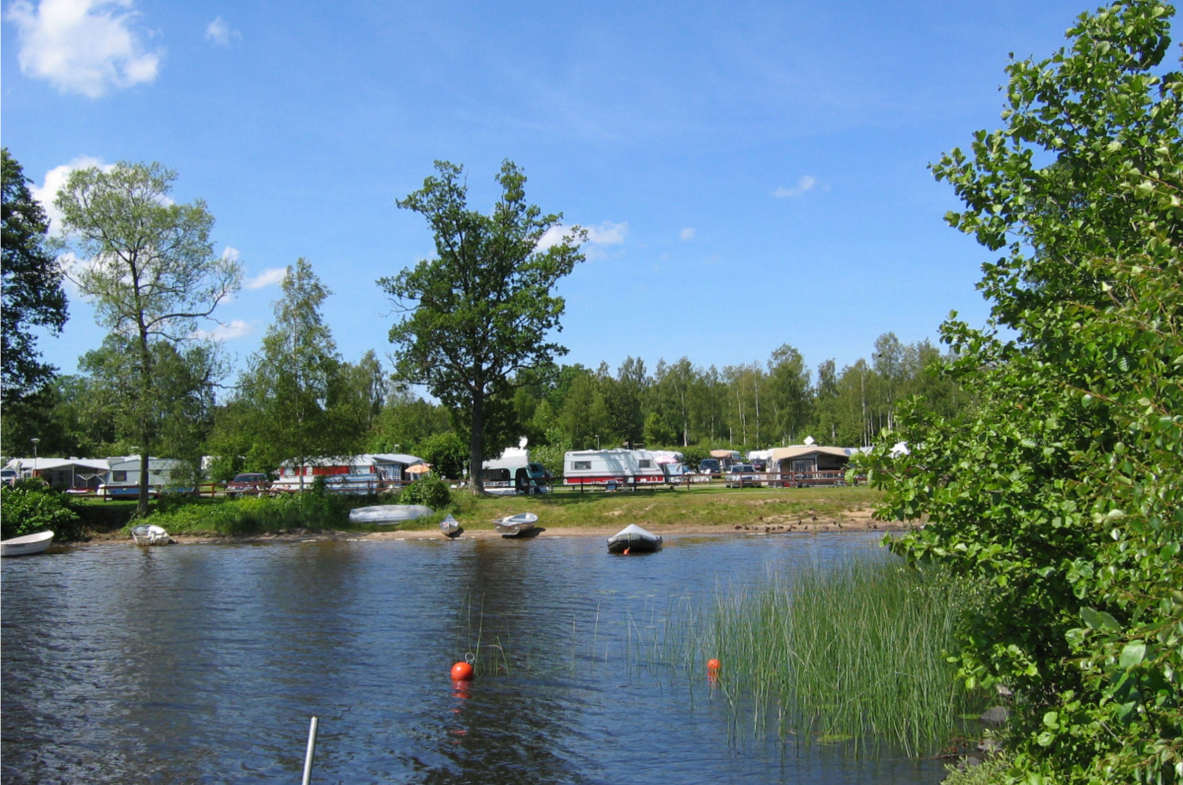 A lakeside campsite with RVs and boats, surrounded by trees and greenery.