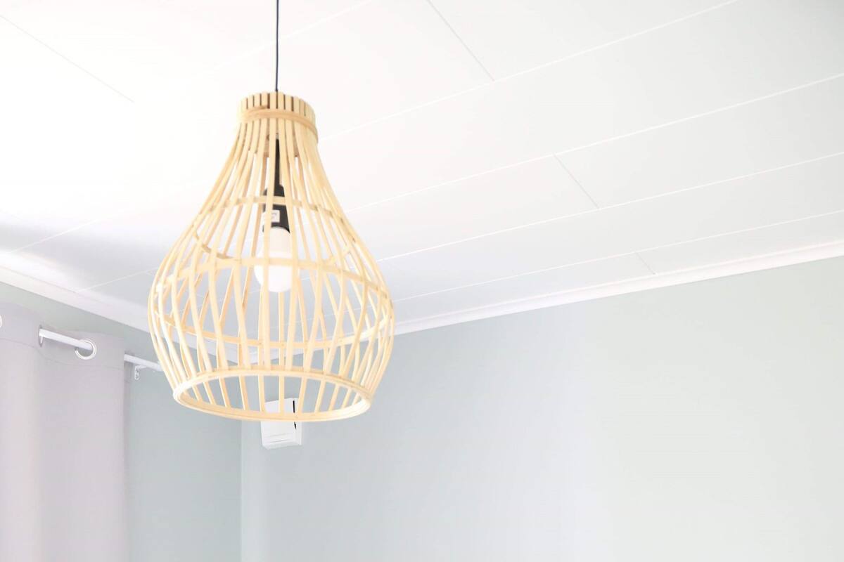 Quarto com cama, luminária pendente e luz fixada na parede.