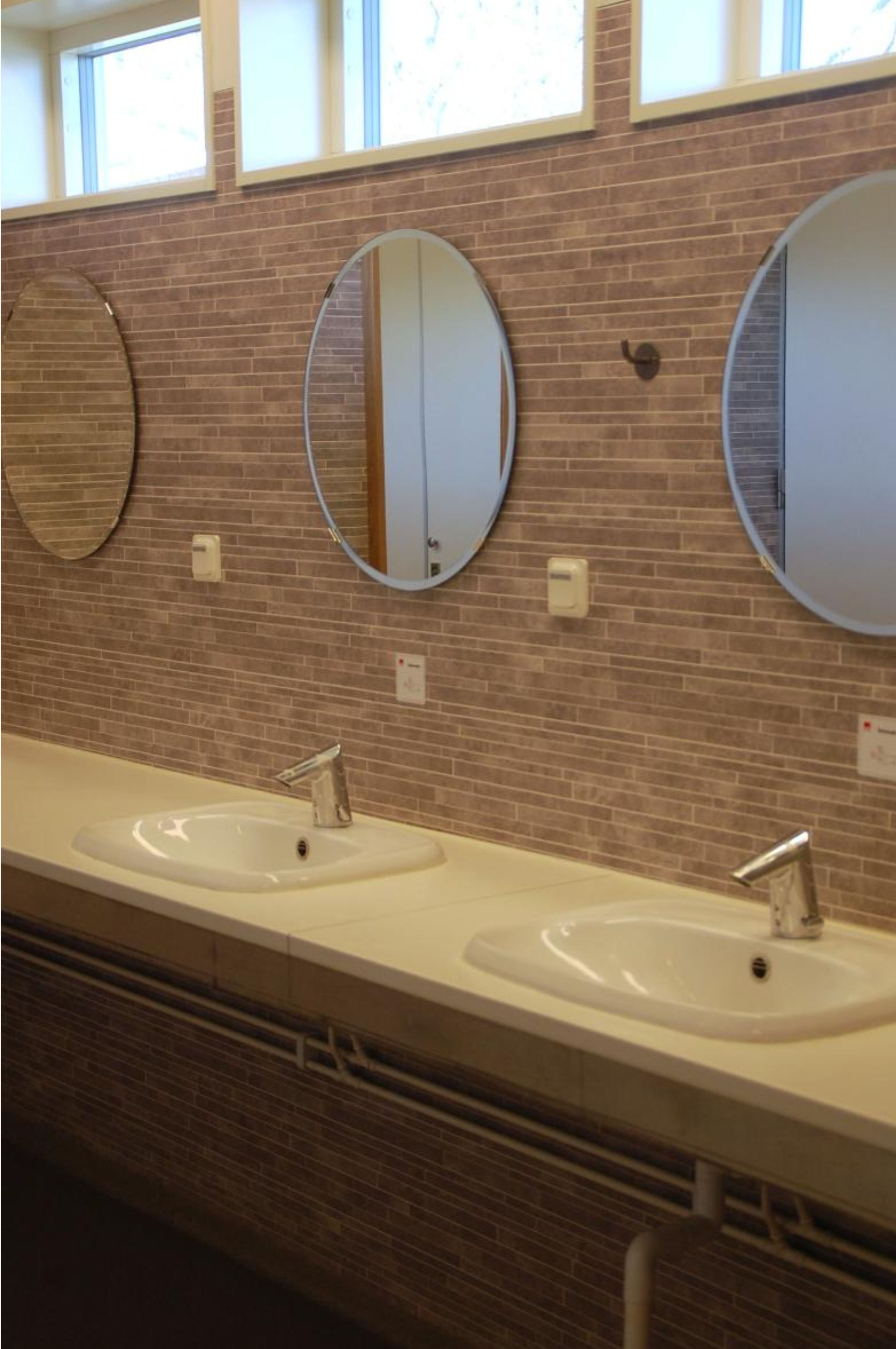 A public restroom with two sinks, three mirrors, and a brick wall.