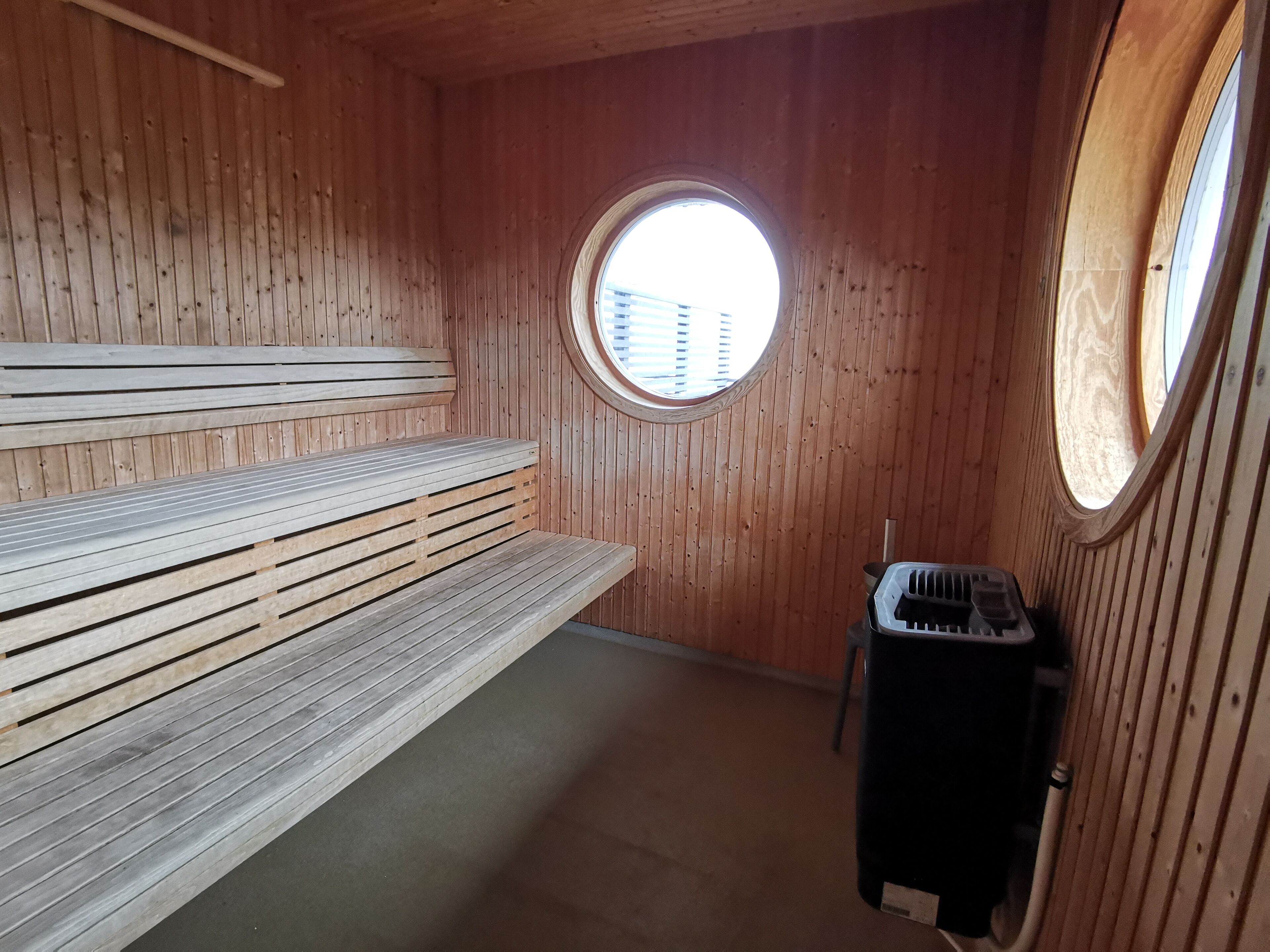 Ein Saunaraum mit Holzbänken, einer Heizung und einem Rundfenster.