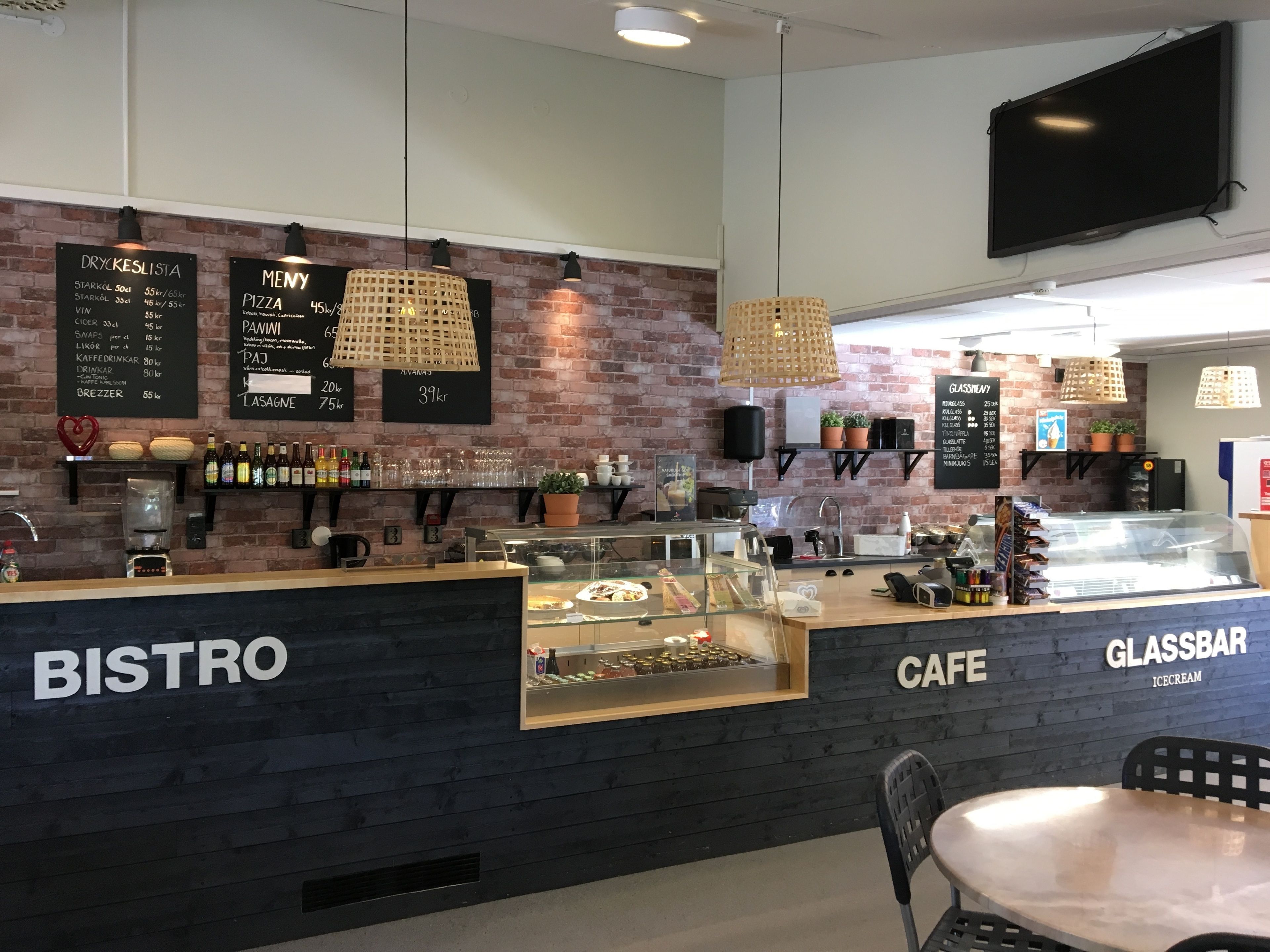 A modern bistro with a brick wall, menu boards, and a glass bar area.