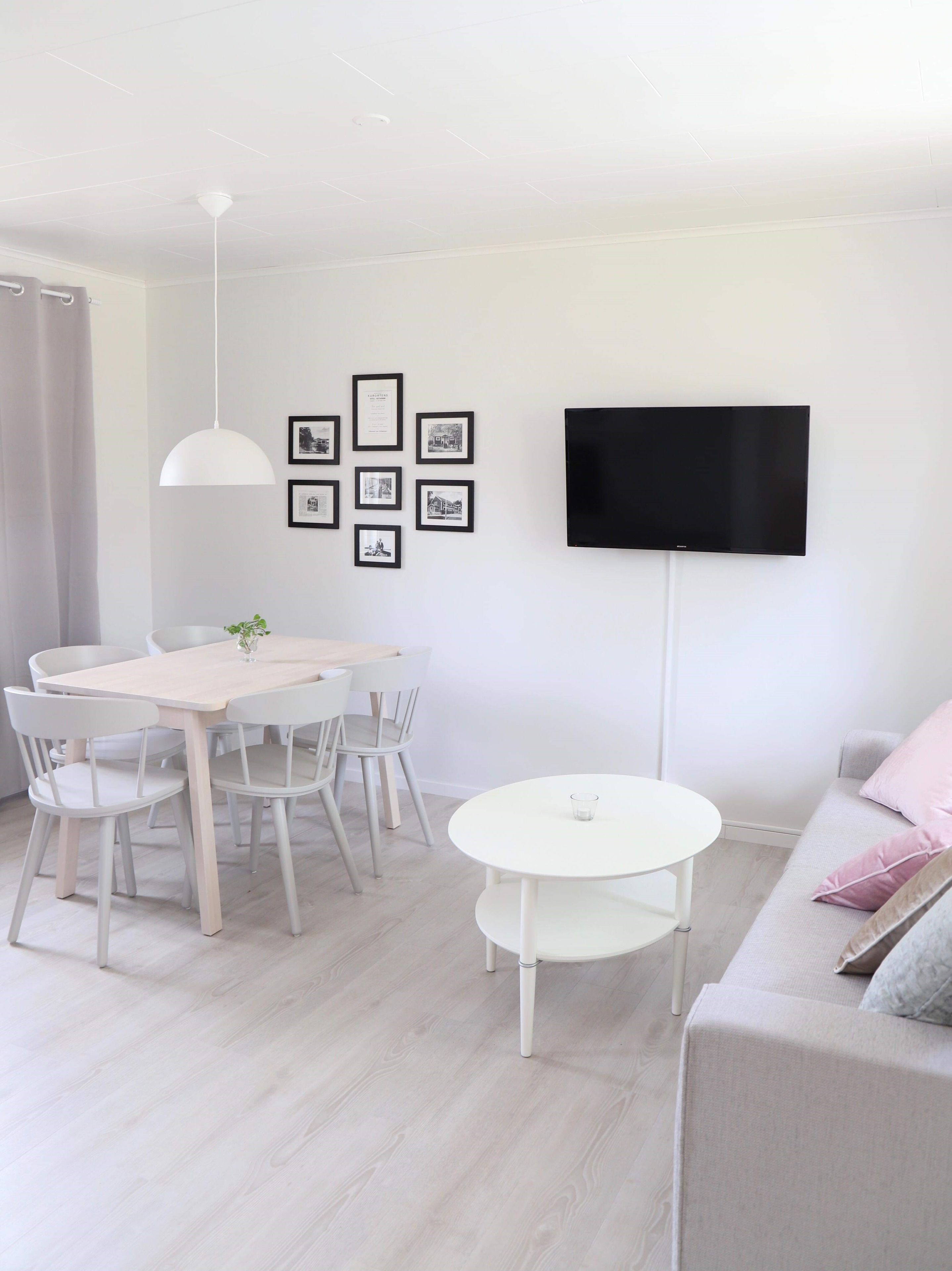 A modern living room with a dining area, a flat-screen TV mounted on the wall, and a minimalist design.