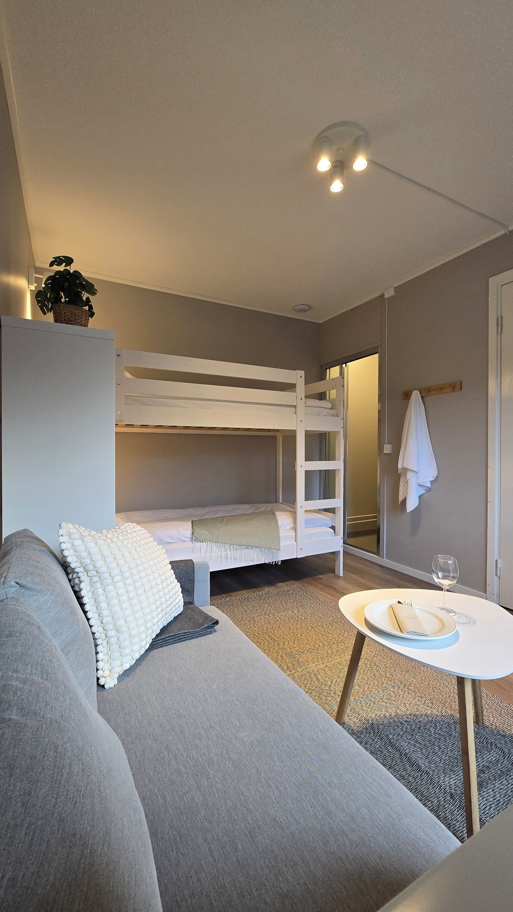A compact room with a bunk bed, a sofa, a small table with a glass of water, and a towel hanging on the wall.