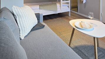 A compact room with a bunk bed, a sofa, a small table with a glass of water, and a towel hanging on the wall.