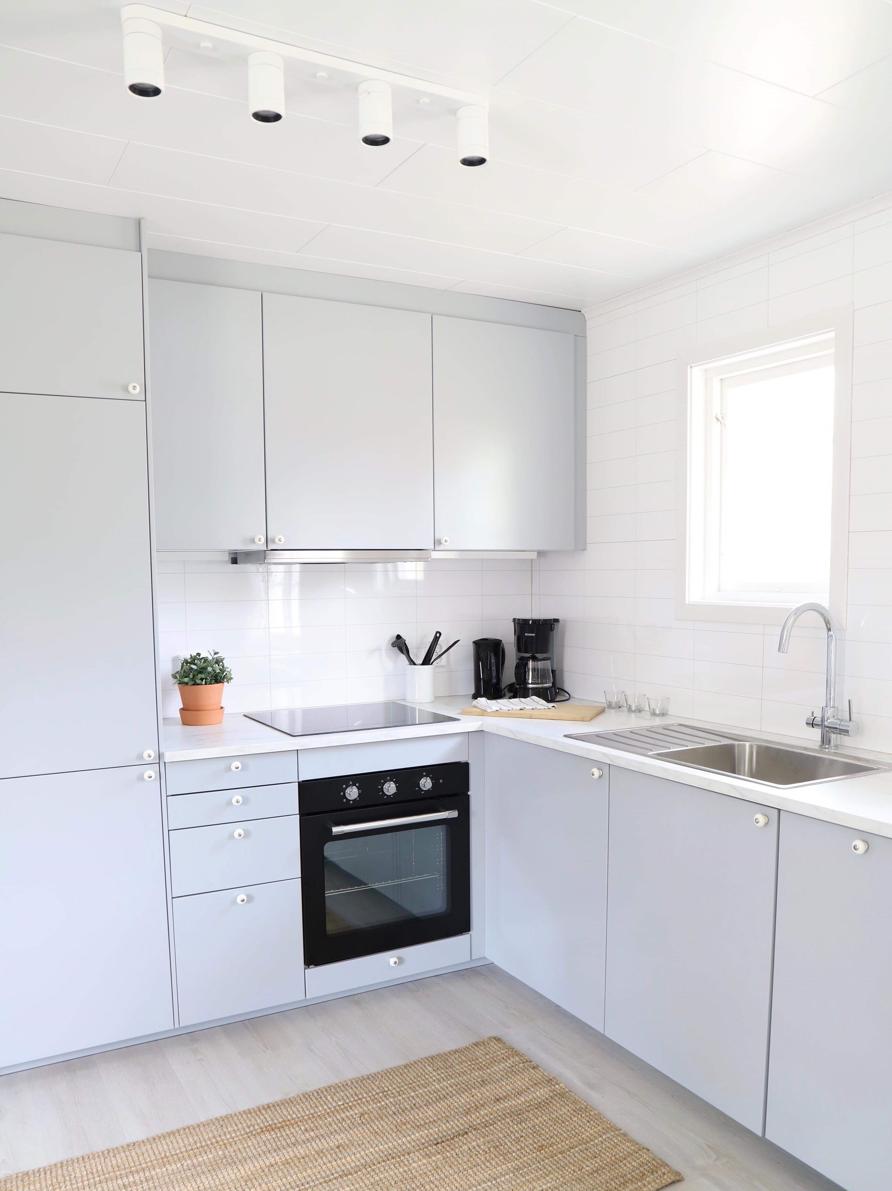 A modern kitchen with white cabinets, a black oven, a coffee maker, and a window.