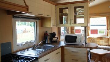 Una cocina compacta con estufa a gas, pileta y microondas. Hay una ventana que proporciona luz natural y vistas al exterior.