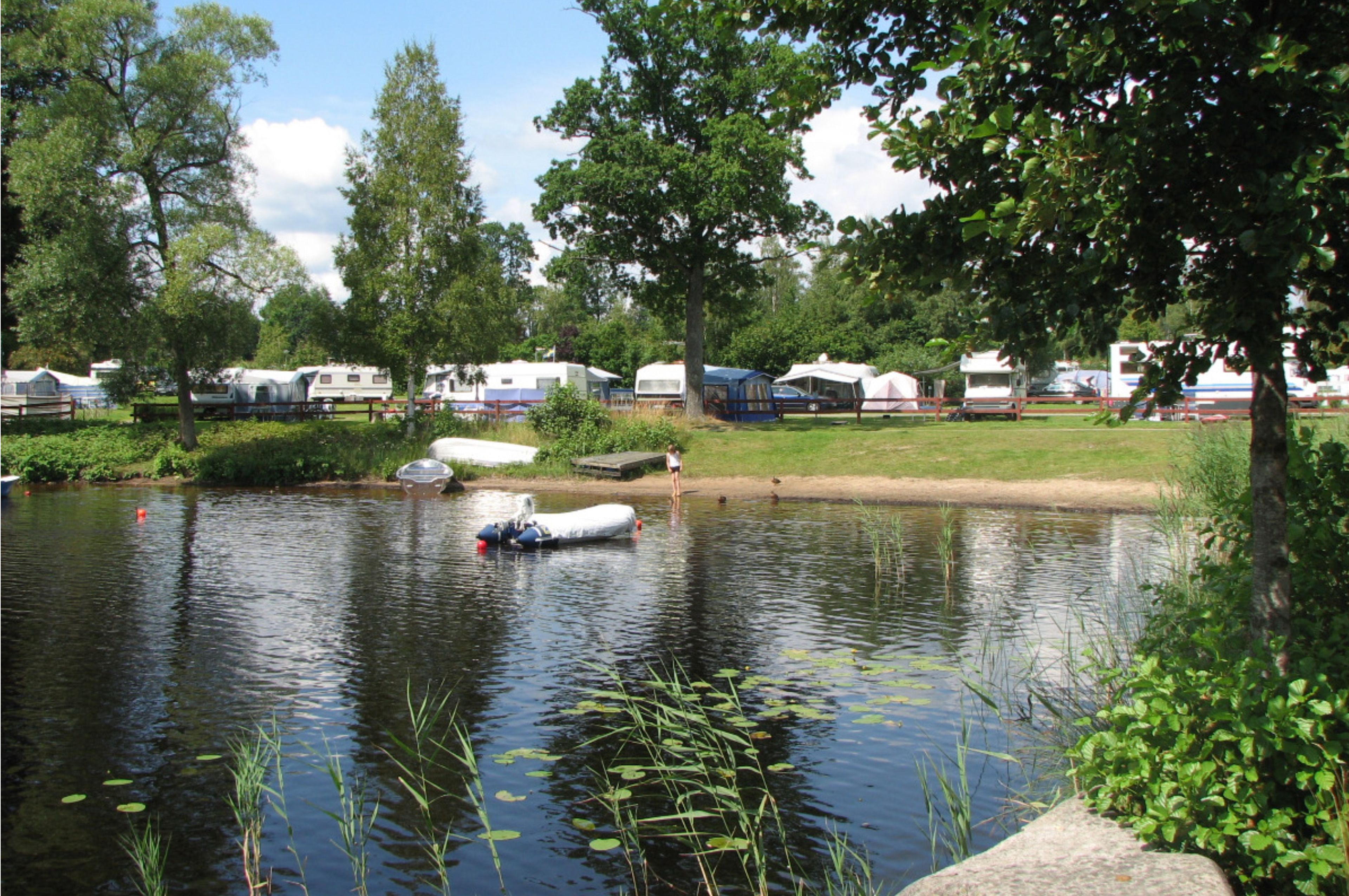 A campsite with RVs and tents near a calm lake, surrounded by trees and greenery.