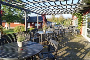 An outdoor patio with tables and chairs, a pergola, and a view of a red building and trees. - Tingsryd Resort (Tingsryd)