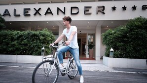 Une personne à vélo devant un bâtiment sur lequel on peut lire l’inscription « ALEXANDER ».