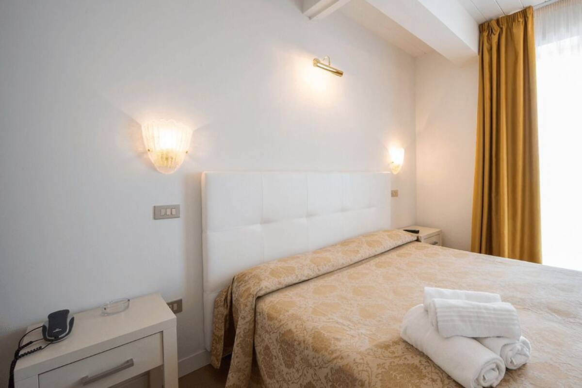 A hotel room with a bed, bedside table, lamp, and curtains.